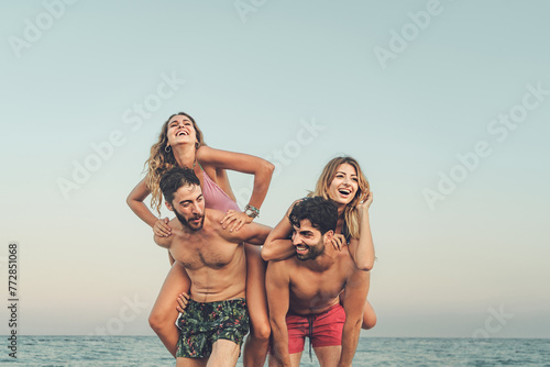 Two couples share laughter with piggyback rides on the beach, embodying the spirit of a carefree and joyful vacation by the sea - beach joy - copy space in the sky