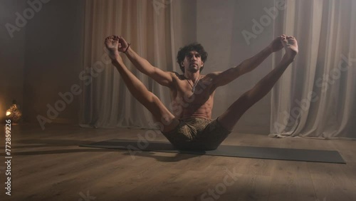 A young man is engaged in yoga exercises spreading his legs apart.