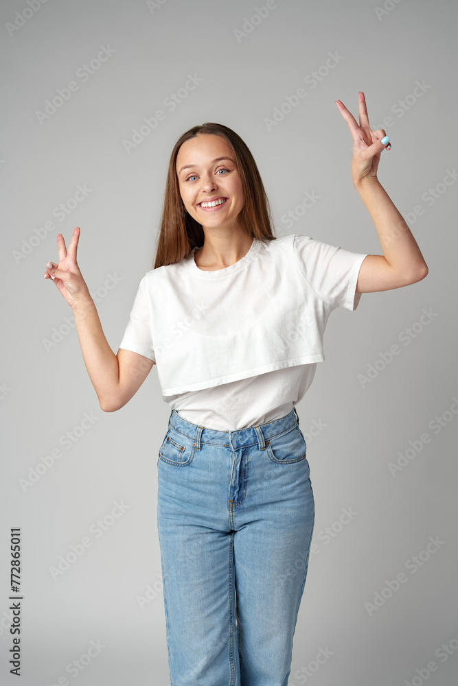 Smiling young woman showing victory sign on gray background Smiling young woman showing victory sign on gray background