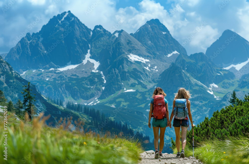 Tatra Mountains summer hiking with friends, two women in colorful and backpacks walking along the path among green grass on a high mountain background