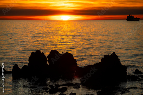 Sunset over the sea with cliffs and oil tanker in the backlight