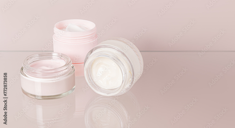 Three open cosmetic jars with cream for everyday self-care on a beige background and a glass surface. Front view. a copy space. Three open cosmetic jars with cream for everyday self-care on a beige background and a glass surface. Front view. a copy space.