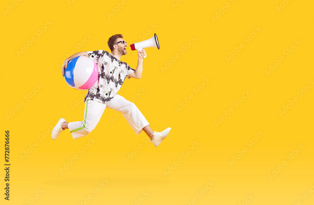 Portrait of a funny young man tourist wearing casual clothes with inflatable beach ball screaming in mouthpiece on studio yellow background and jumping. Vacation trip and summer holiday concept.