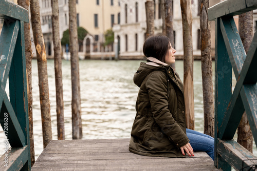 Young female tourist sitting on a dock in Venice while taking in the scenery and enjoying her trip in the Italian city.