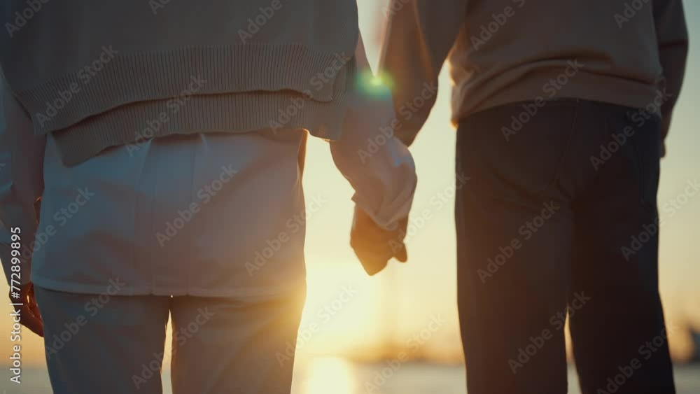 Hands of elderly people at sunset. Married old positive couple man woman holding hands and walking along the seashore together, back view. Long-marriage love, family support, summer vacation concept. Hands of elderly people at sunset. Married old positive couple man woman holding hands and walking along the seashore together, back view. Long-marriage love, family support, summer vacation concept.