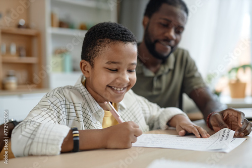 Portrait of smiling Black boy doing homework at kitchen table with father helping copy space