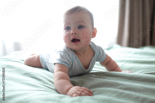 4-5 Monthe old baby lies on a sheet in bed and builds different emotional faces, smileas, studies his legs grabbing them with his hands. Textiles and family bed linen photo