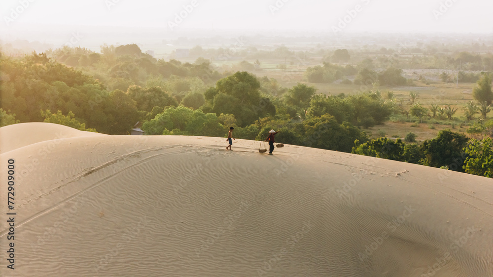 Aerial view of a peasant woman carries a bamboo frame on the shoulder across sand dunes in Ninh Thuan province, Vietnam. It is one of the most beautiful places in Vietnam