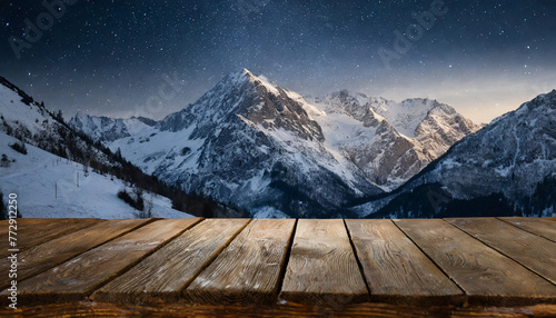 Empty wooden deck table against view of snowy mountain range in the night.