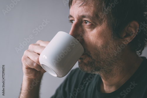 Unkempt man drinking morning coffee from a white mug