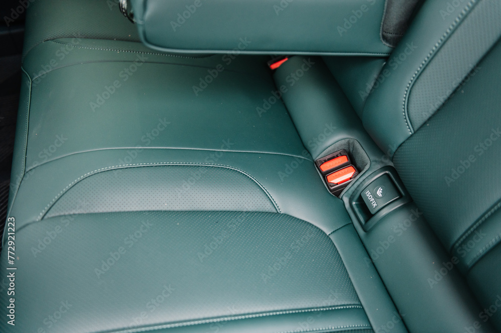 Installing ISOFIX baby and car seat for maximum safety. Part of green perforated leather car seat. Fastening child seat with isofix system. Luxury car inside. Interior of prestige modern electric car.