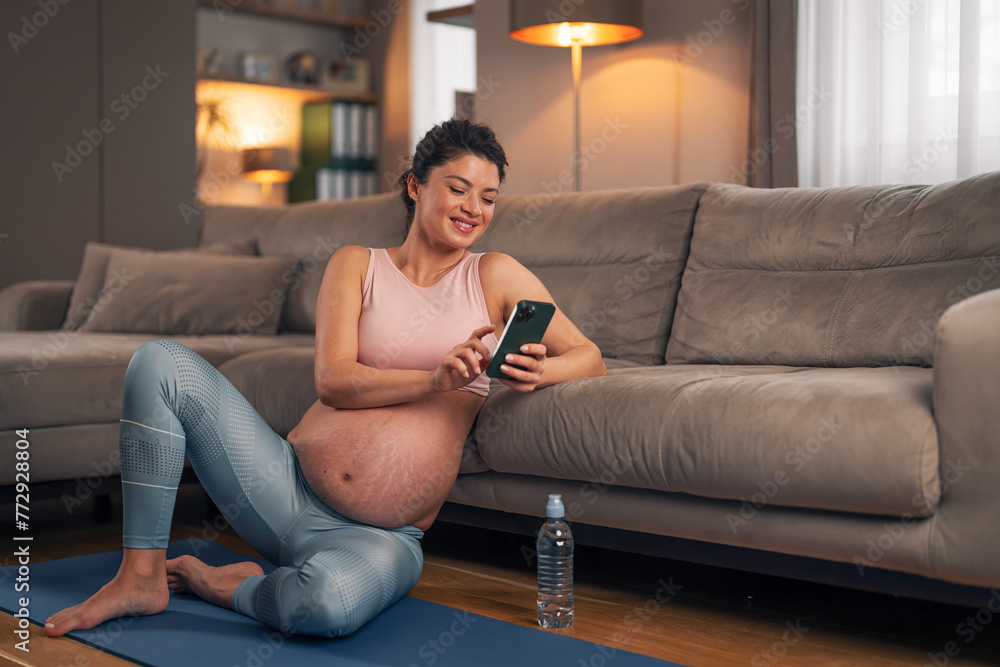 Obraz premium A happy pregnant woman scrolling through her phone while taking a break from her home workout