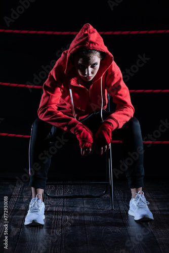 The athlete sits in a chair in the boxing ring after losing the fight. Despite the technical preparation, the athlete lost the fight in a sweatshirt.