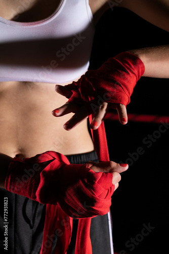 The athlete wraps her hands with a boxing bandage. Preparation for an important fight. The woman focused during the last steps before going to the ring. © fotodrobik