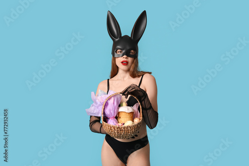 Sexy young woman in bunny mask with basket for Easter on blue background