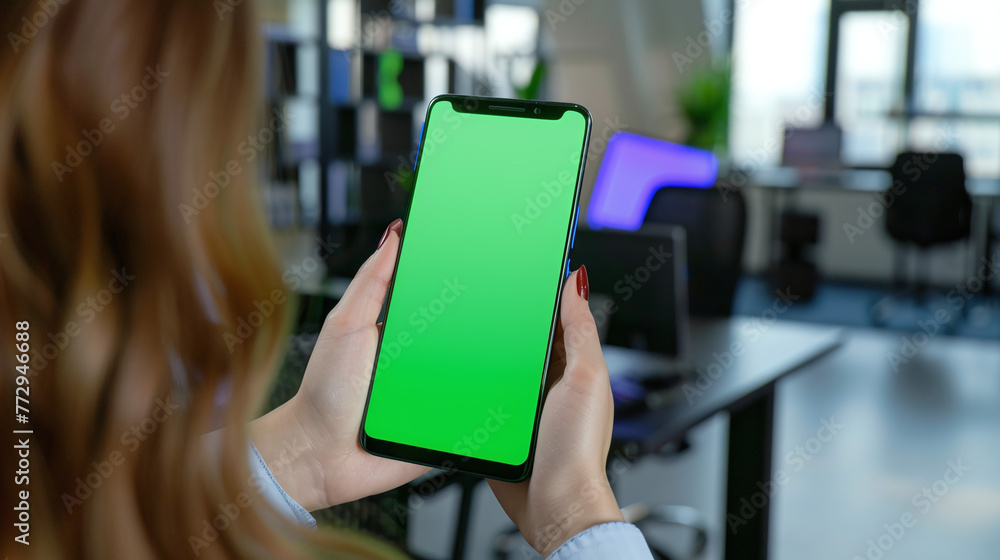 Woman holding smartphone with blank green screen on office background Woman holding smartphone with blank green screen on office background