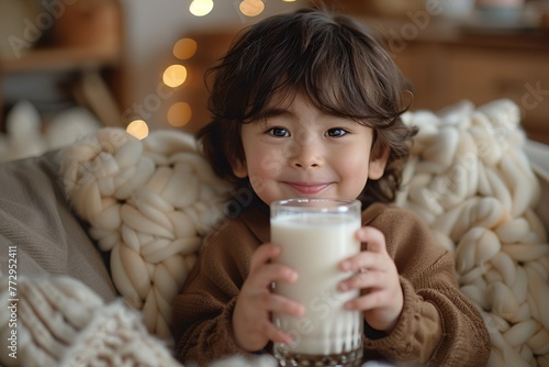 Smiling cute baby holding a glass of milk, promoting health and growth.