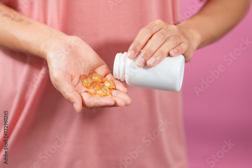 A professional image showcasing a female hand delicately holding a bottle of cod liver oil with her fingers against a soft pink isolated background.