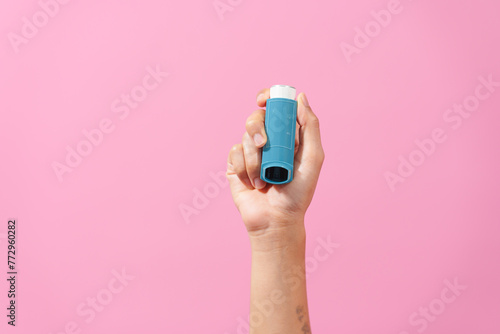A professional image featuring a female hand holding an asthma inhaler with fingers against a soft pink isolated background, highlighting respiratory health and wellness. photo