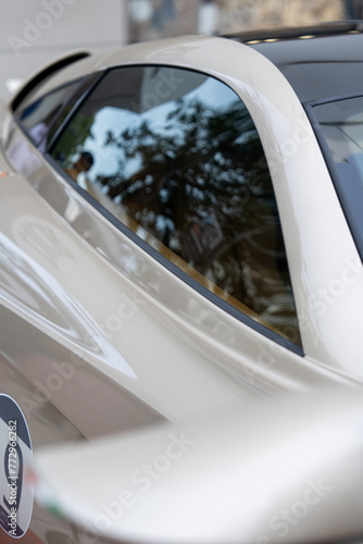 Focus on side glass of coupe sports car with shiny neutral surface. Sample of new auto model exhibited outdoors with number sticker on door