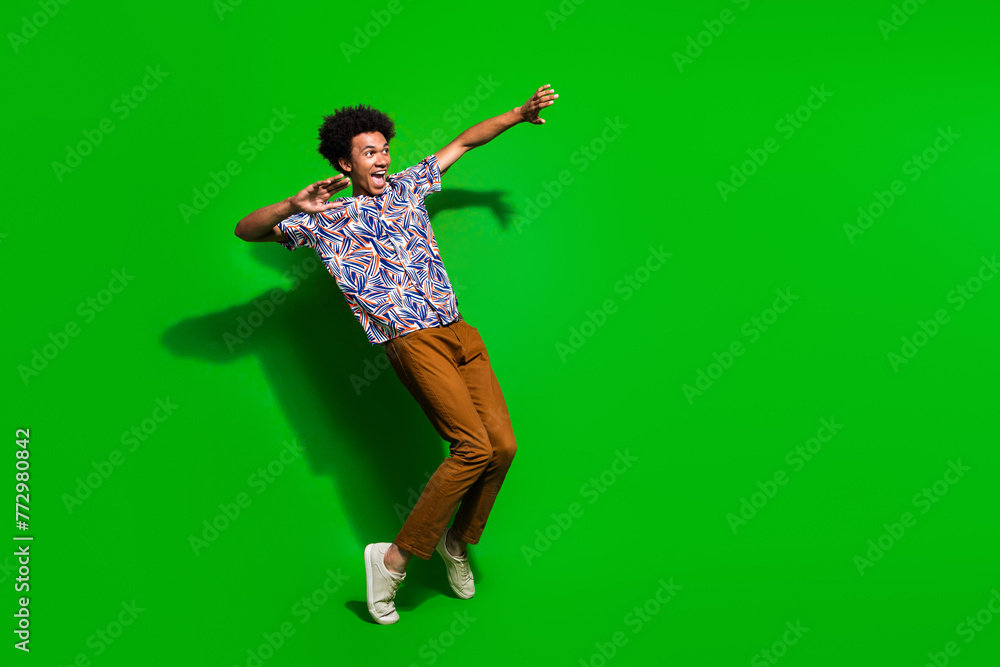 Full length photo of attractive funky guy wear print shirt enjoying discotheque empty space isolated green color background Full length photo of attractive funky guy wear print shirt enjoying discotheque empty space isolated green color background