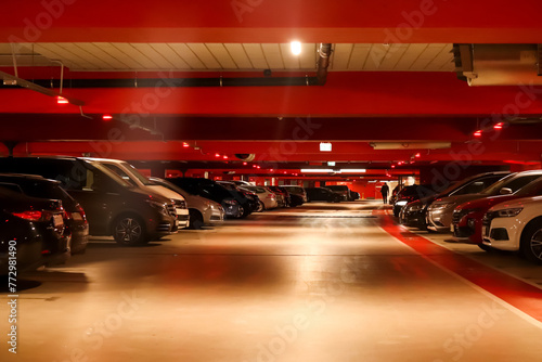Underground parking garage with cars parked and illuminated by red lights, suitable for illustrating safety measures during emergencies or promoting secure parking facilities. Blurred