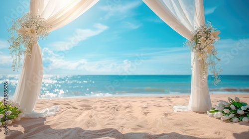 A beach wedding setup with a white draped arch decorated with flowers on a sunny seaside