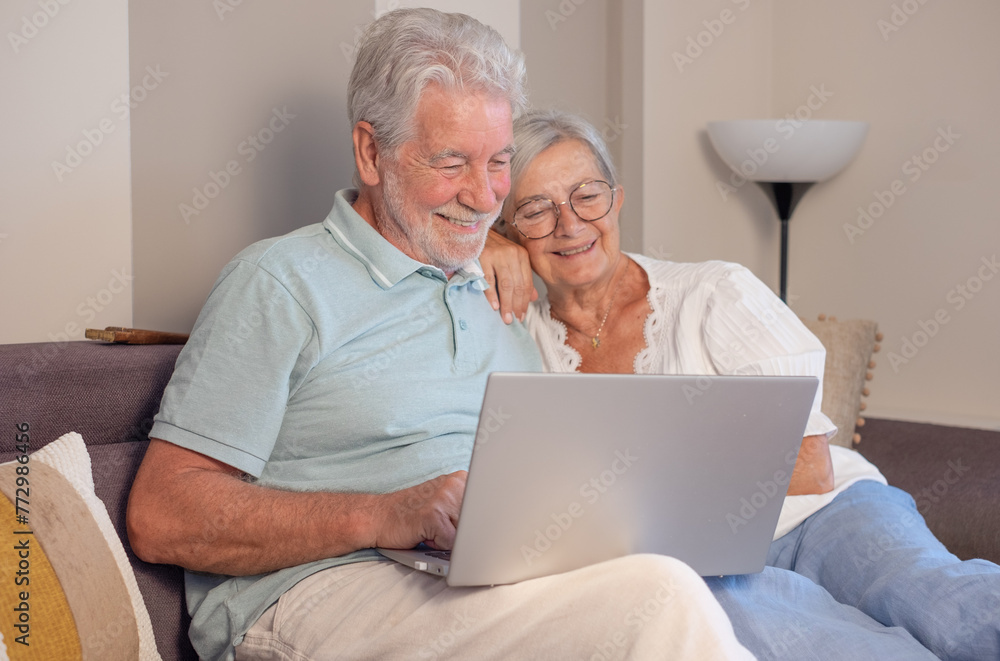 Cheerful senior couple relaxing on sofa, using laptop technology, enjoying happy moments together in good mood and harmony Cheerful senior couple relaxing on sofa, using laptop technology, enjoying happy moments together in good mood and harmony