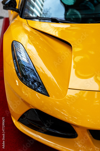 Stunning design of super car parked outdoors painted in vibrant yellow color. Electric headlight located on relief bonnet with additional air intake openings for powerful rides