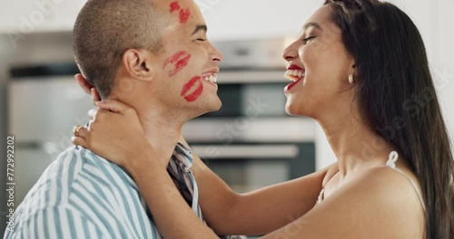 Happy couple, love and kiss with lipstick for fun date and playful at home in intimacy, romance and valentines day. Lover, woman and man in kitchen or house with lip print on cheek for anniversary photo
