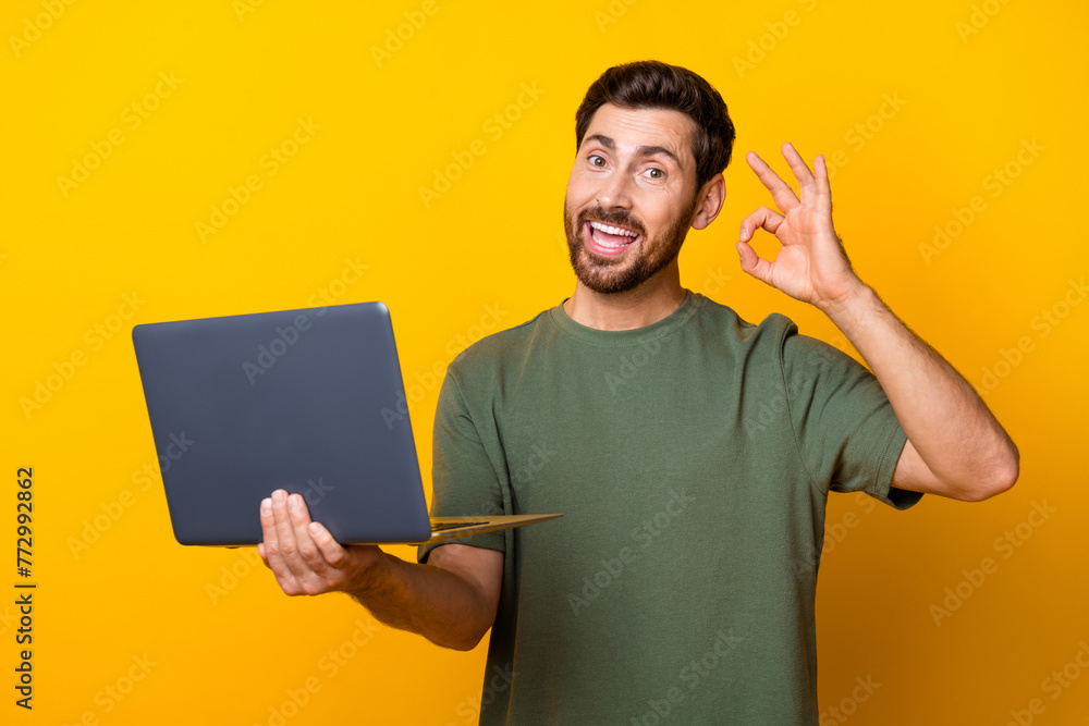 Fototapeta premium Photo portrait of handsome young guy hold netbook show okey symbol dressed stylish khaki outfit isolated on yellow color background