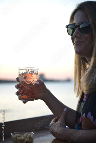 giovane donna beve un cocktail al tramonto in riva al mare
