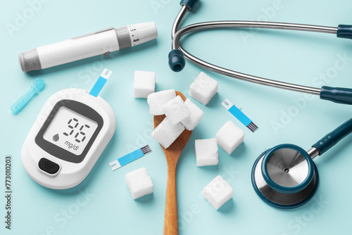 Sugar cubes in spoon with blood glucose meter, lancet and stethoscope on blue background