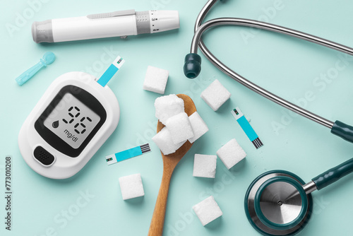 Sugar cubes in spoon with blood glucose meter, lancet and stethoscope on green background, diabetes concept