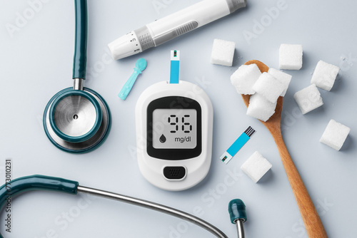 Blood glucose meter with stethoscope and sugar cubes in spoon on table, diabetes concept