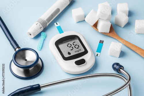Blood glucose meter with stethoscope and sugar cubes in spoon on green background, diabetes concept