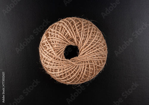 A brown ball of yarn is sitting on a black surface. The yarn is twisted and knotted, giving it a rough and unkempt appearance. Concept of nostalgia and simplicity, as the yarn represents a basic