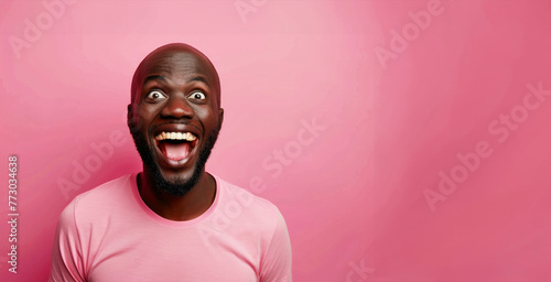 A man with a big smile on his face is wearing a pink shirt. He is looking at the camera and he is happy. Bald black guy smiling with mouth closed, eyes wide and excited of winning a prize © Nataliia_Trushchenko