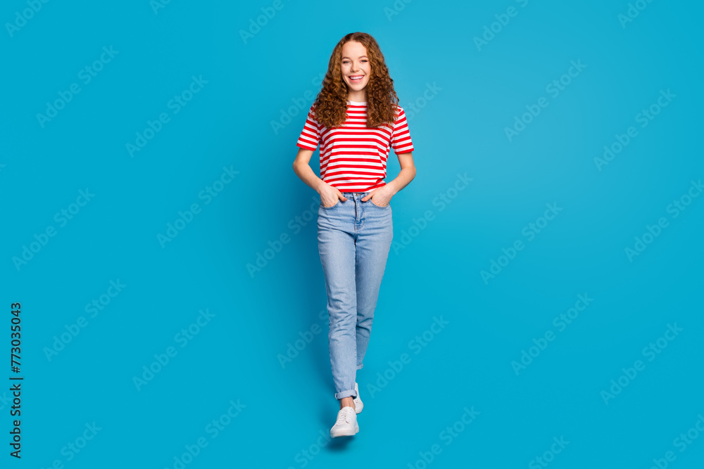 Full length photo of cheerful woman dressed striped t-shirt jeans standing keep palms in pockets isolated on blue color background Full length photo of cheerful woman dressed striped t-shirt jeans standing keep palms in pockets isolated on blue color background