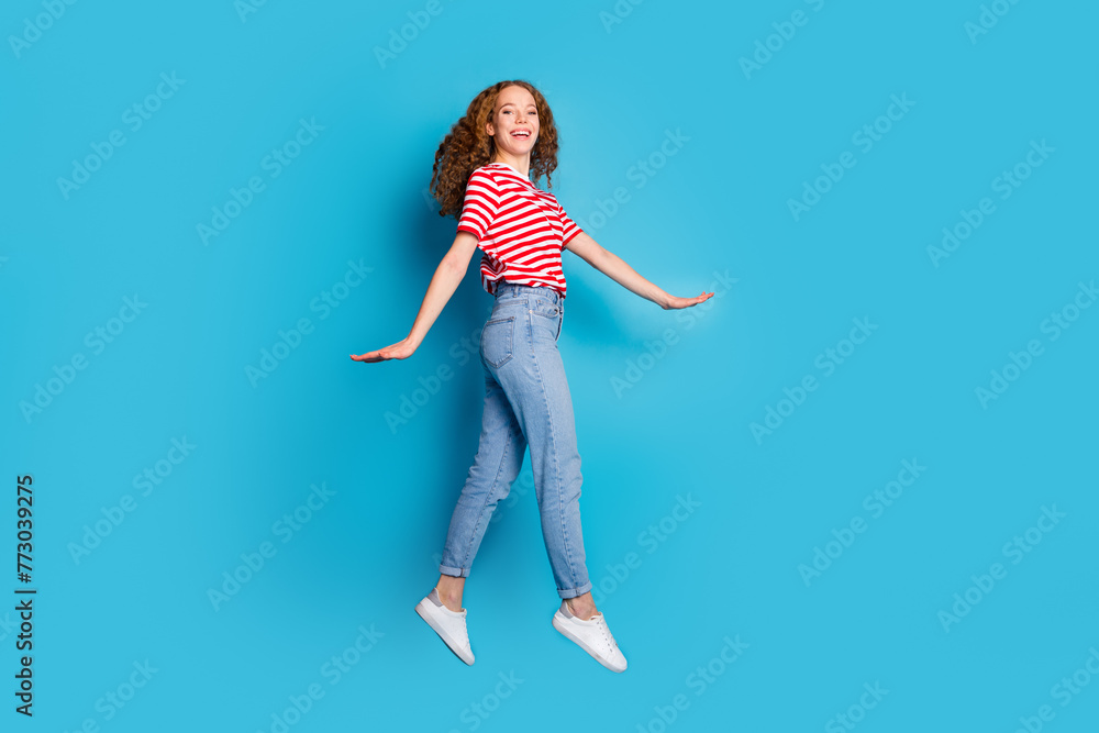 Full length photo of adorable lovely positive woman dressed striped t-shirt jeans flying having fun isolated on blue color background