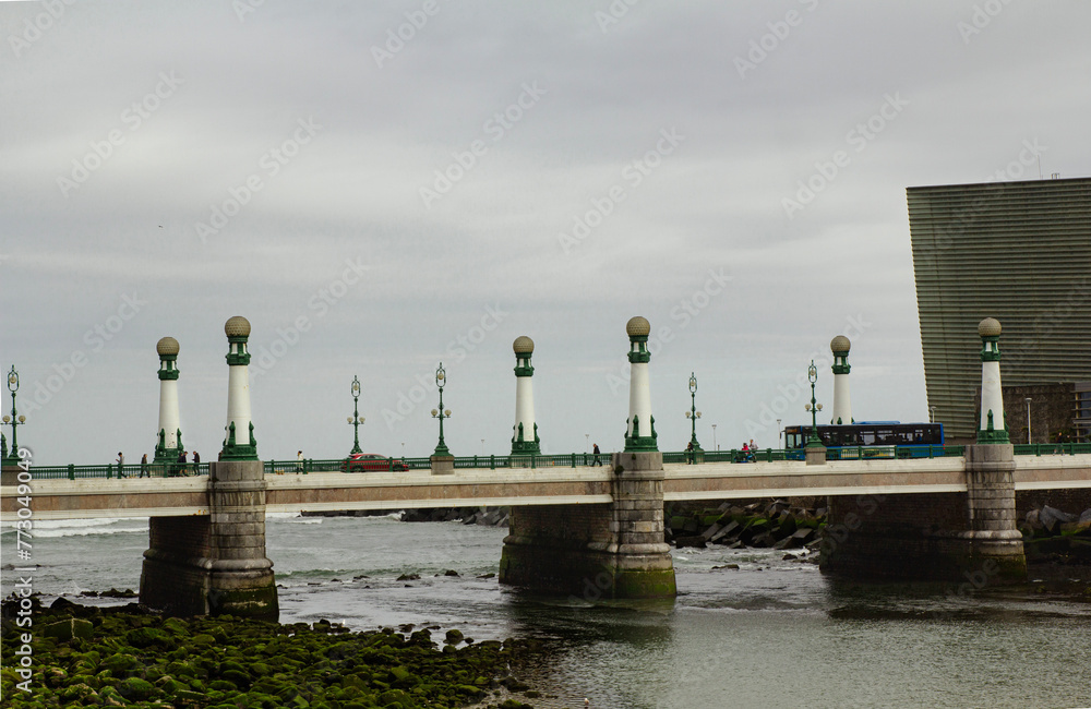 Fototapeta premium Beautiful bridge with lanterns over the Urumea river. San Sebastian, Spain. Beautiful bridge with lanterns over the Urumea river. San Sebastian, Spain. It's a nasty day
