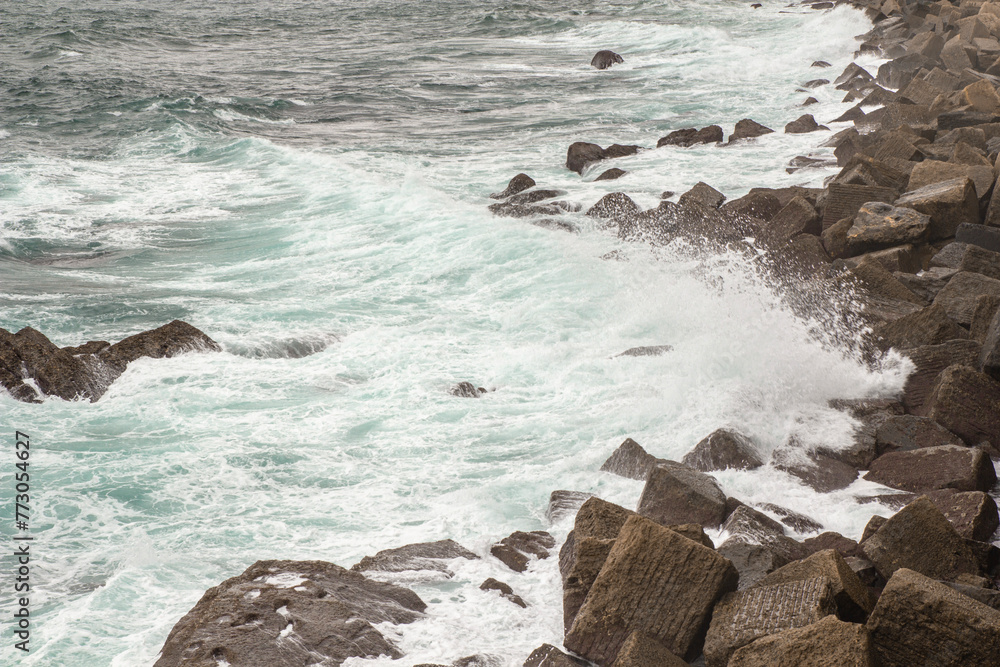 Fototapeta premium Ocean waves crash against the rocky shore. San Sebastian, Spain. Cloudy spring day