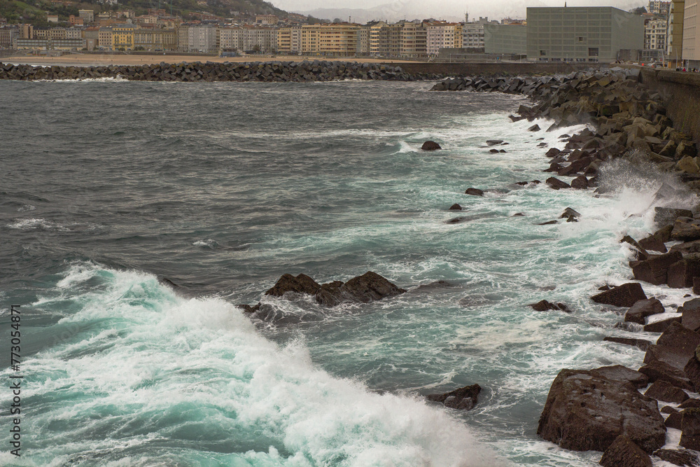 Naklejka premium Ocean waves crash against the rocky shore. San Sebastian, Spain. Cloudy spring day
