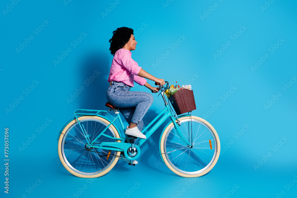 Full length side profile photo of active girl dressed shirt jeans riding bike look at sale empty space isolated on blue color background Full length side profile photo of active girl dressed shirt jeans riding bike look at sale empty space isolated on blue color background