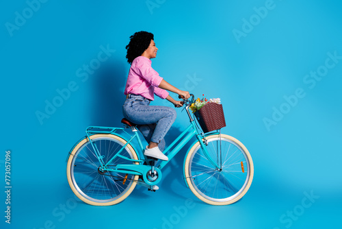 Fototapeta Naklejka Na Ścianę i Meble -  Full length side profile photo of active girl dressed shirt jeans riding bike look at sale empty space isolated on blue color background