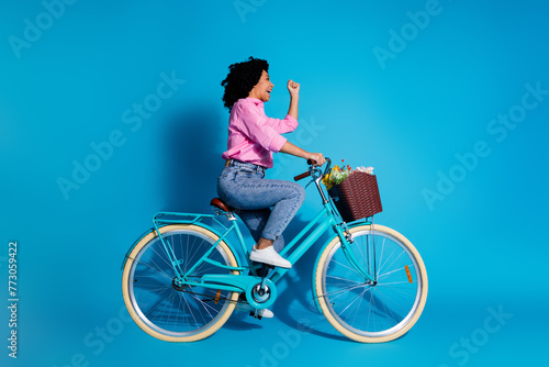 Fototapeta Naklejka Na Ścianę i Meble -  Full length side profile photo of excited girl dressed shirt riding bike look empty space clenching fist isolated on blue color background