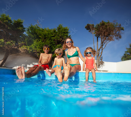 Happy family by the poolside smiling dangling legs in warm pool