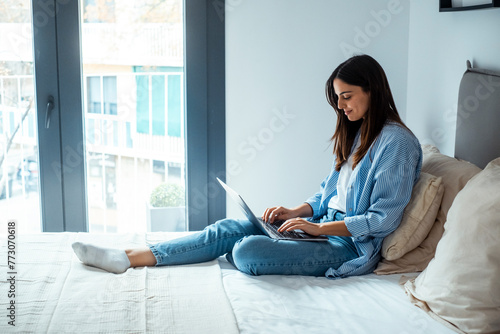 One young lady having relax surfing the net alone at home sitting on bed in bedroom. Traveler business modern online people working in hotel room. One woman using computer laptop with relaxation photo
