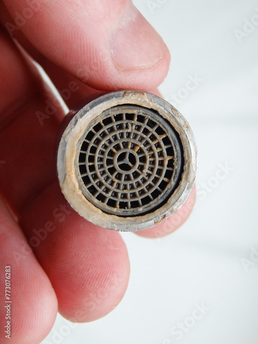 Hand is holding a chrome faucet aerator covered with lime scale. Faucet contaminated with calcium. Limescale on tap mixer. photo