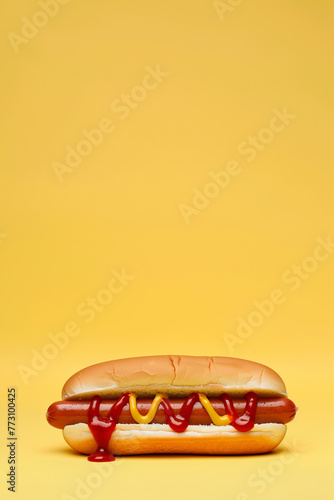 photo of a Hot Dog on a bun, white bread roll with ketchup and mustard on a plain yellow background with copy space